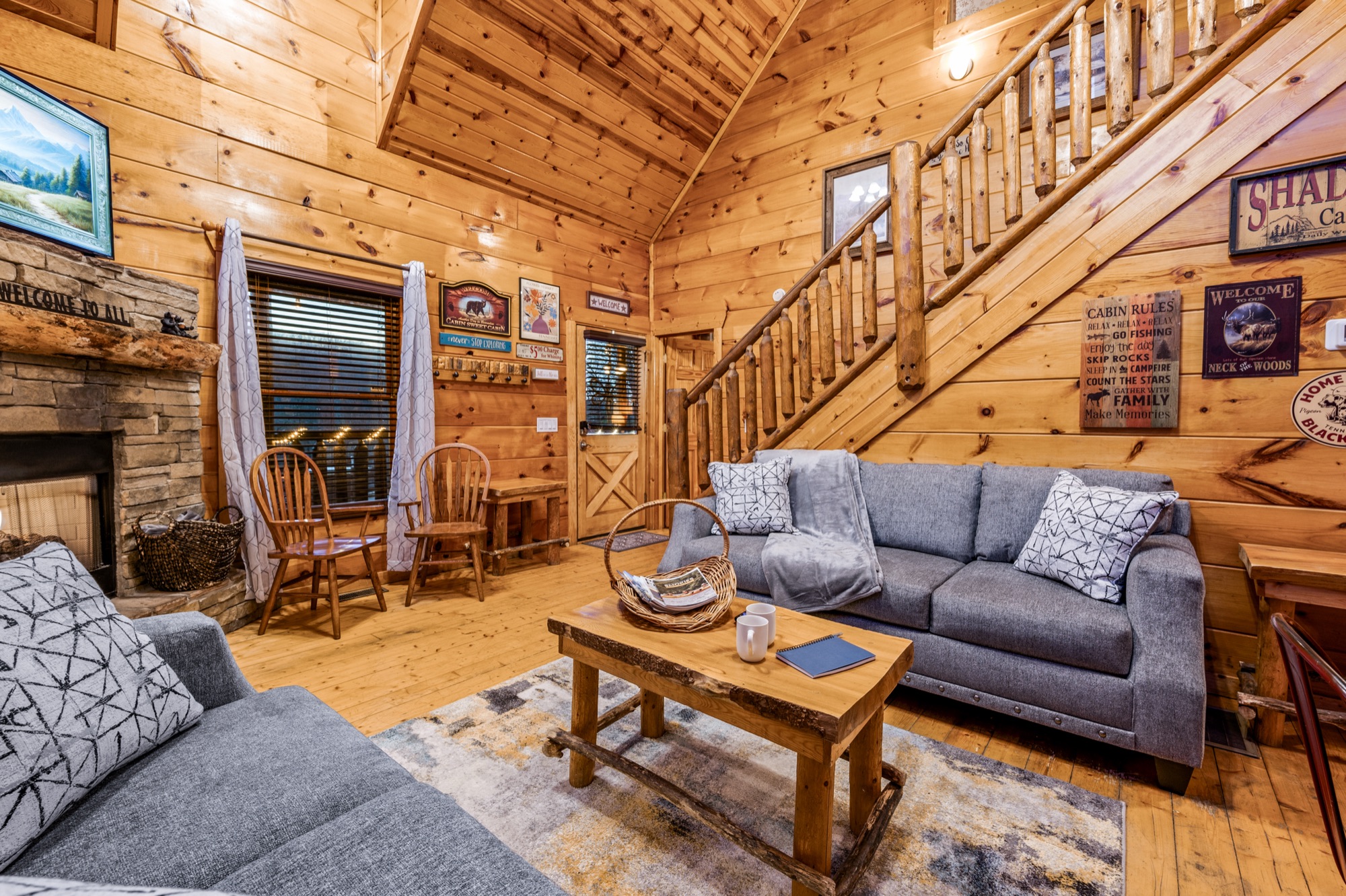 Bearadise living room with log stairs to the loft, a stone fireplace, and a Cabin Rules sign